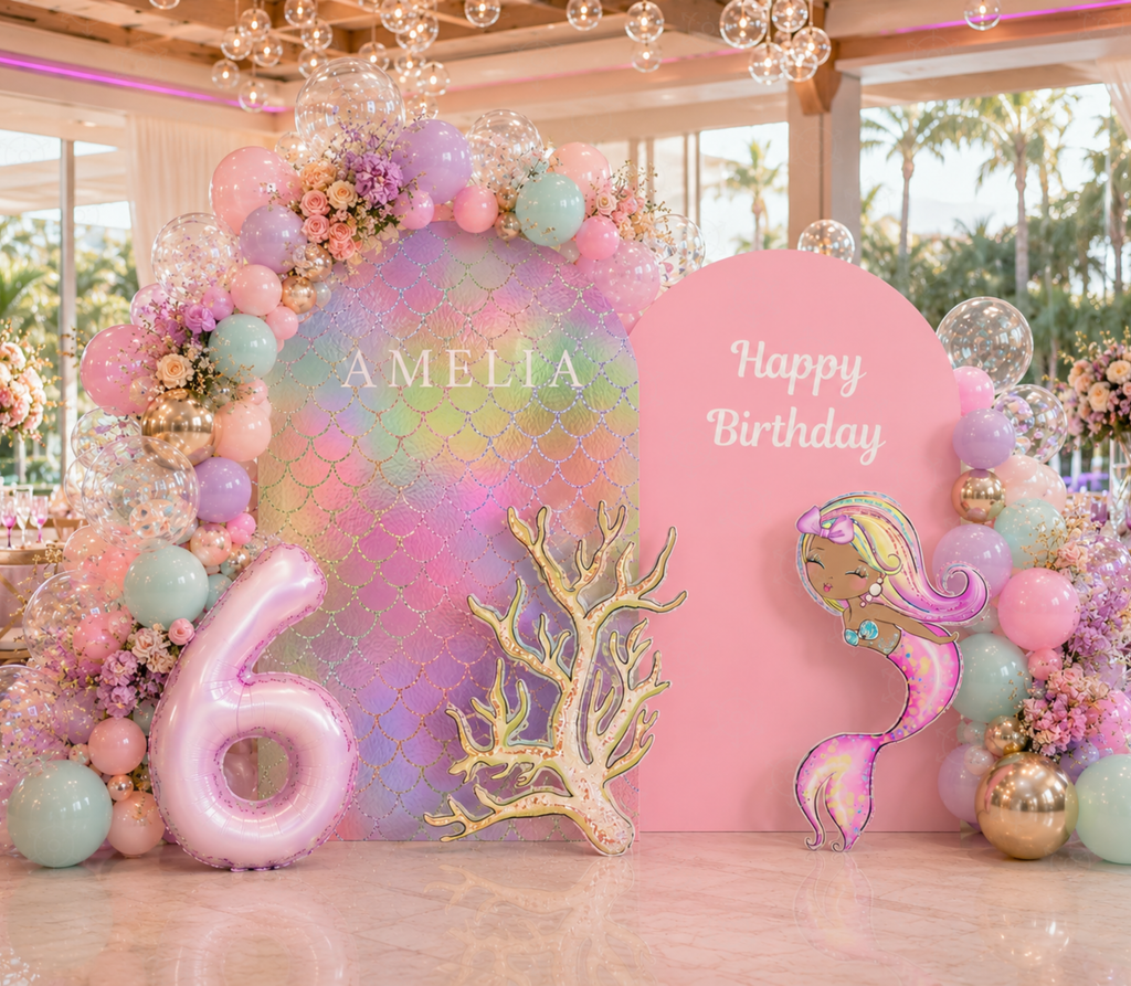 Pink and purple mermaid birthday backdrop with pastel balloon garland, ocean cutouts and personalized under the sea party decor.