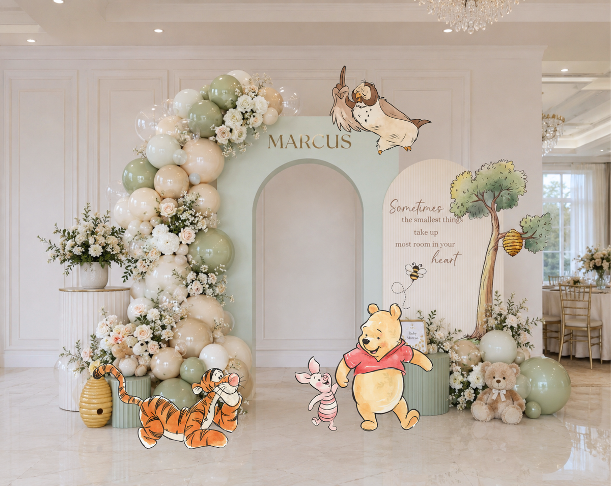 Pastel woodland baby shower backdrop with blue arch panel, tree details and classic bear inspired character cutouts.