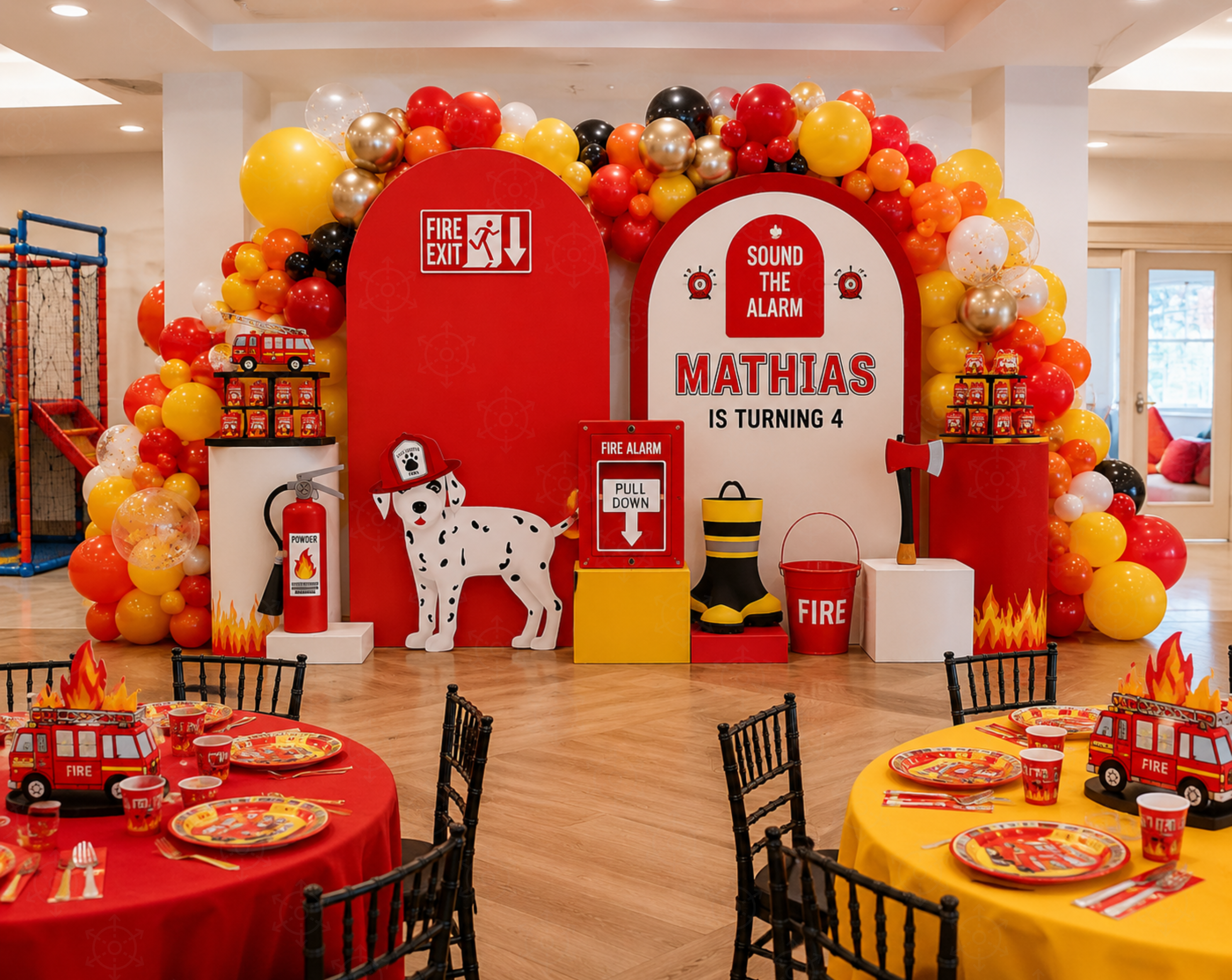 Indoor firefighter party entrance with a red house-shaped arch, dalmatian cutout, balloon decor and a fire truck centerpiece.