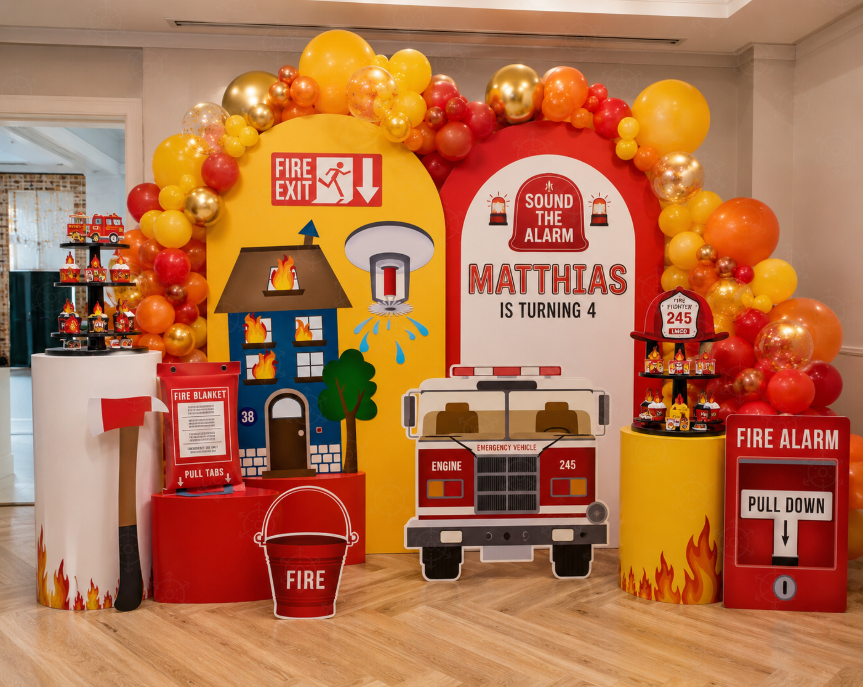 Personalized fire station birthday backdrop with a red arch panel, number accents, fire hydrant prop, balloon clusters and matching party tables.