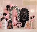 Personalized pink fashion doll birthday backdrop with black and hot pink balloon garland, glam vanity details and matching doll cutouts for a girls party.