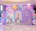 Personalized unicorn birthday backdrop with pastel rainbow arch, unicorn cutouts, pink purple balloons and colorful party decorations.