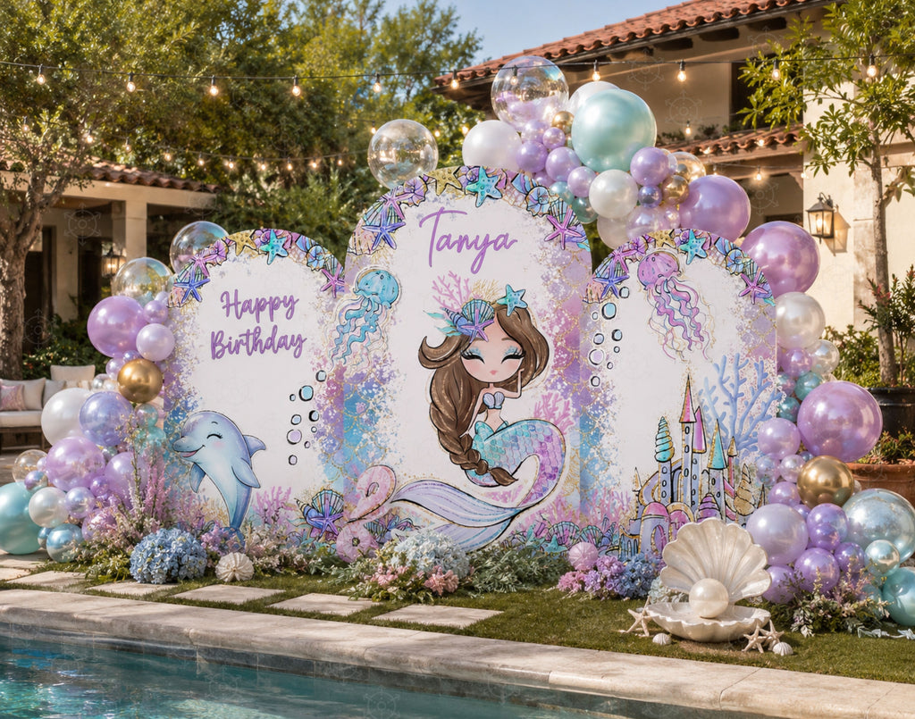 Outdoor mermaid birthday backdrop with floral balloon garland, pastel ocean colors and personalized under the sea party decorations.