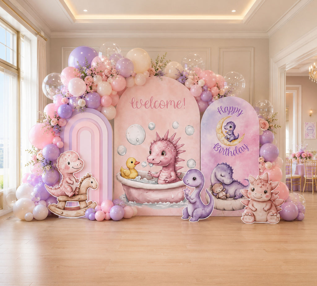 Pastel baby dinosaur birthday backdrop with pink and lavender panels, balloon garland and sweet dino party decorations indoors.