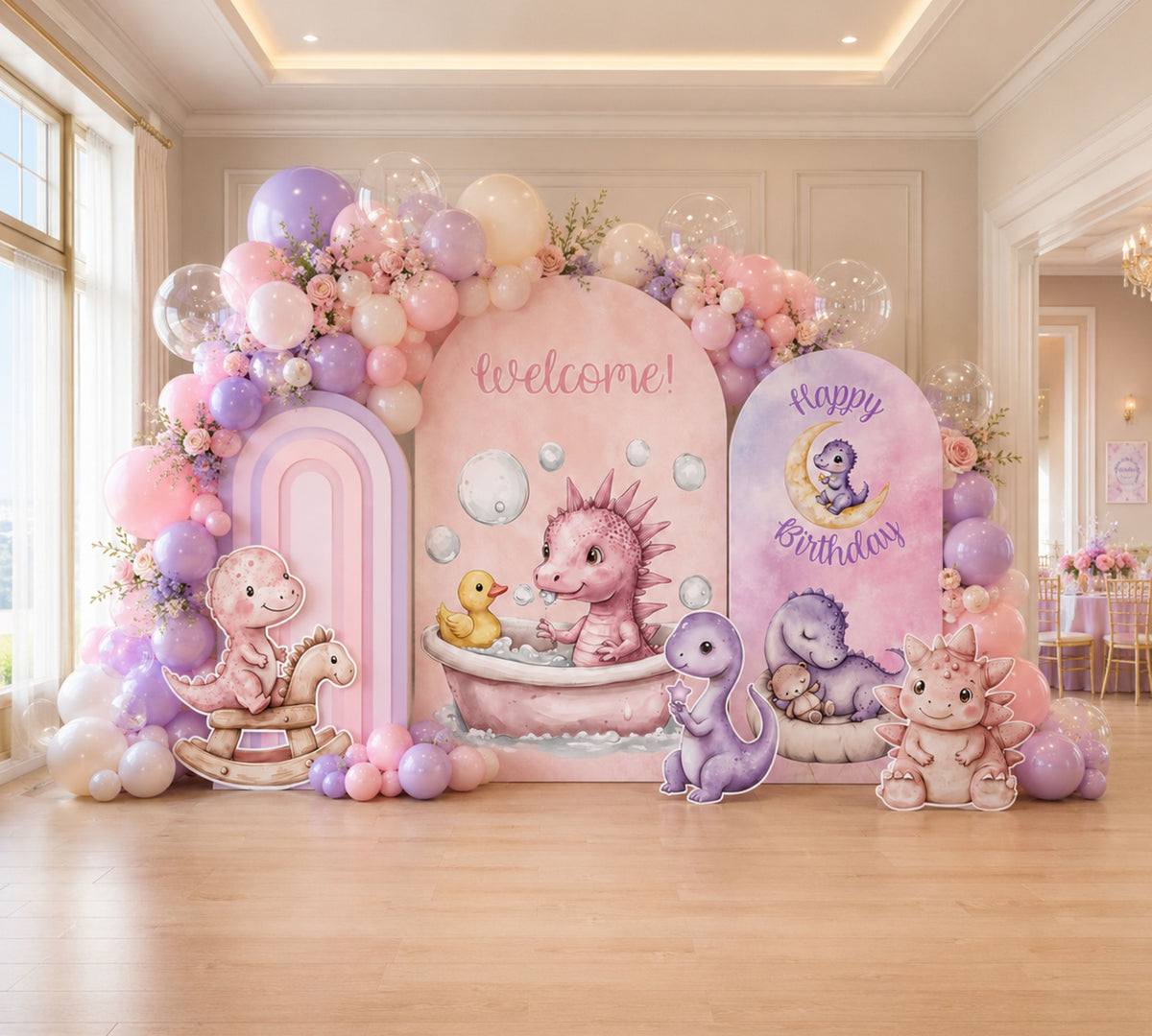 Pastel baby dinosaur birthday backdrop with pink and lavender panels, balloon garland and sweet dino party decorations indoors.