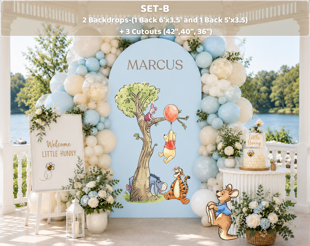 Woodland baby shower backdrop with blue arch panel, tree illustration, white balloons and classic bear inspired party decorations.