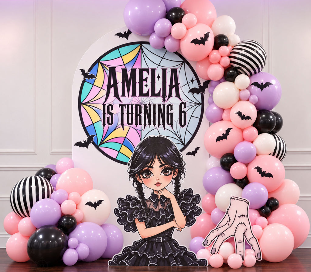 Personalized gothic birthday backdrop with pink and black balloon garland, character cutouts and dramatic birthday styling.