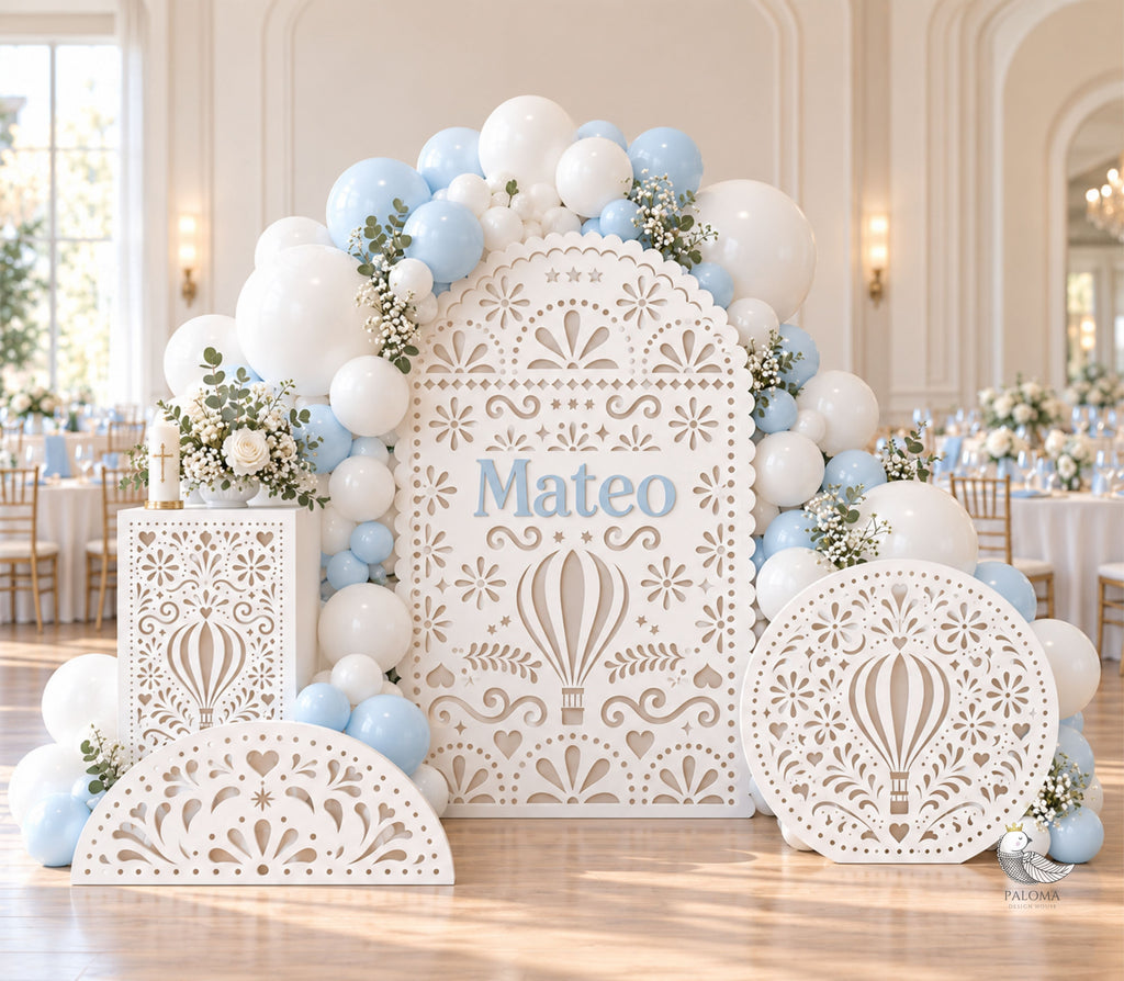 White papel picado baptism backdrop set with personalized Mateo sign, matching pedestal, circle and half circle decor, styled with light blue and white balloons.