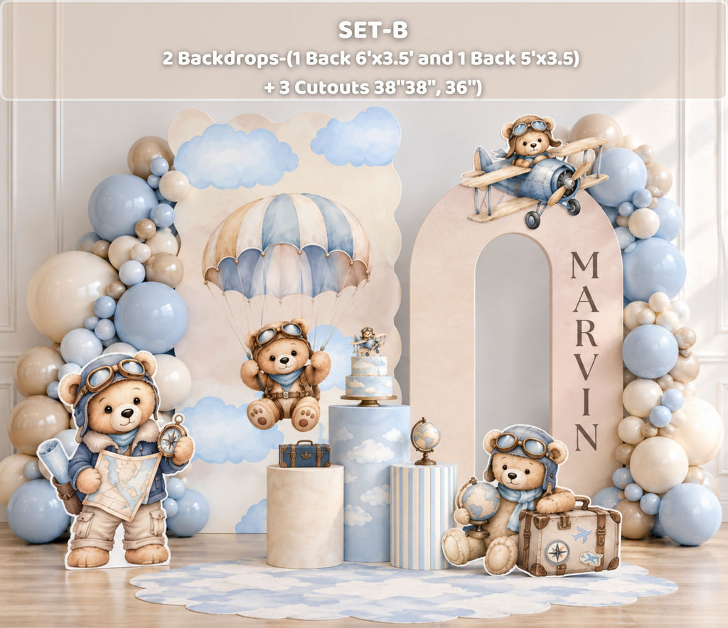 Aviator bear birthday backdrop with light blue arch panels, beige and gold balloon decor, themed bear cutouts and elegant baby boy party styling.