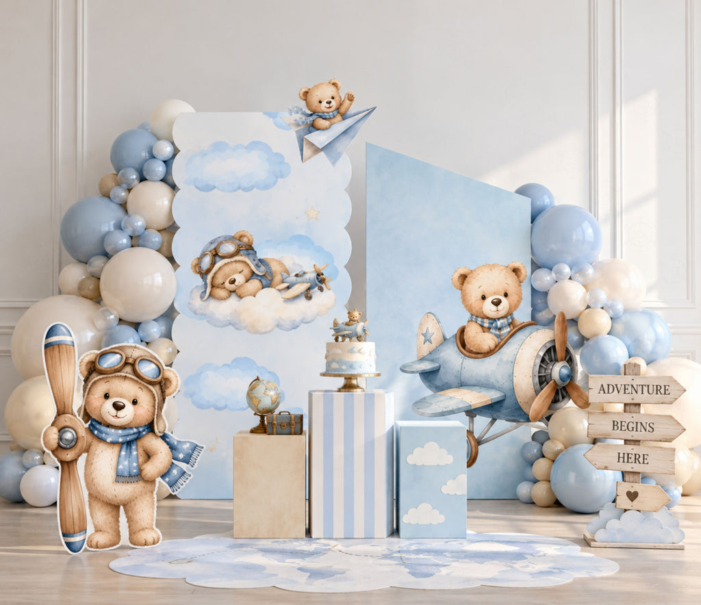 Aviator bear birthday backdrop with blue shelving display, neutral balloon garland, teddy bear accents and coordinated baby boy party decor.