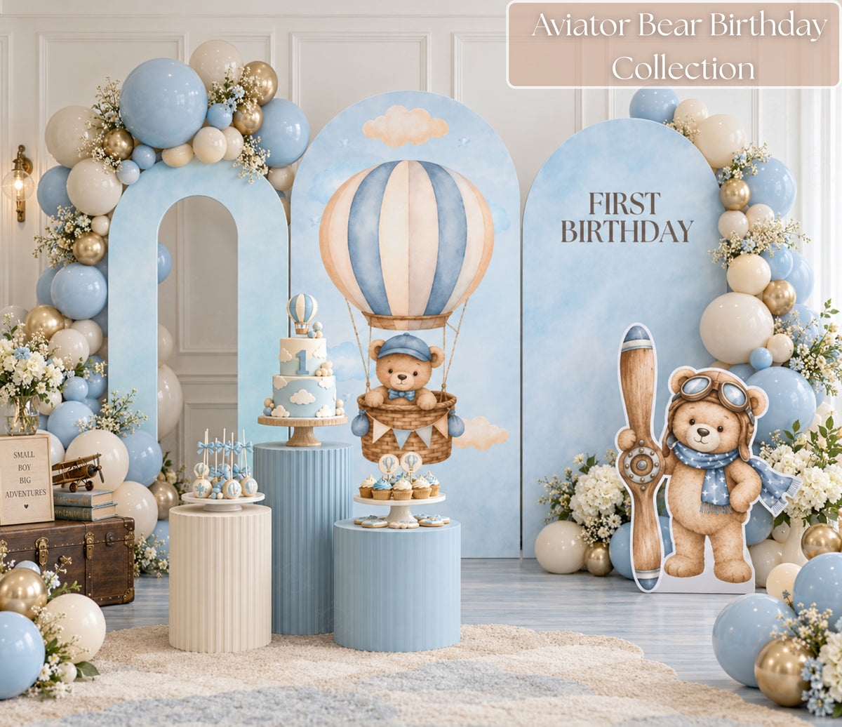 Neutral blue aviator bear birthday backdrop with arched panels, beige balloon garland and matching teddy bear party decor.