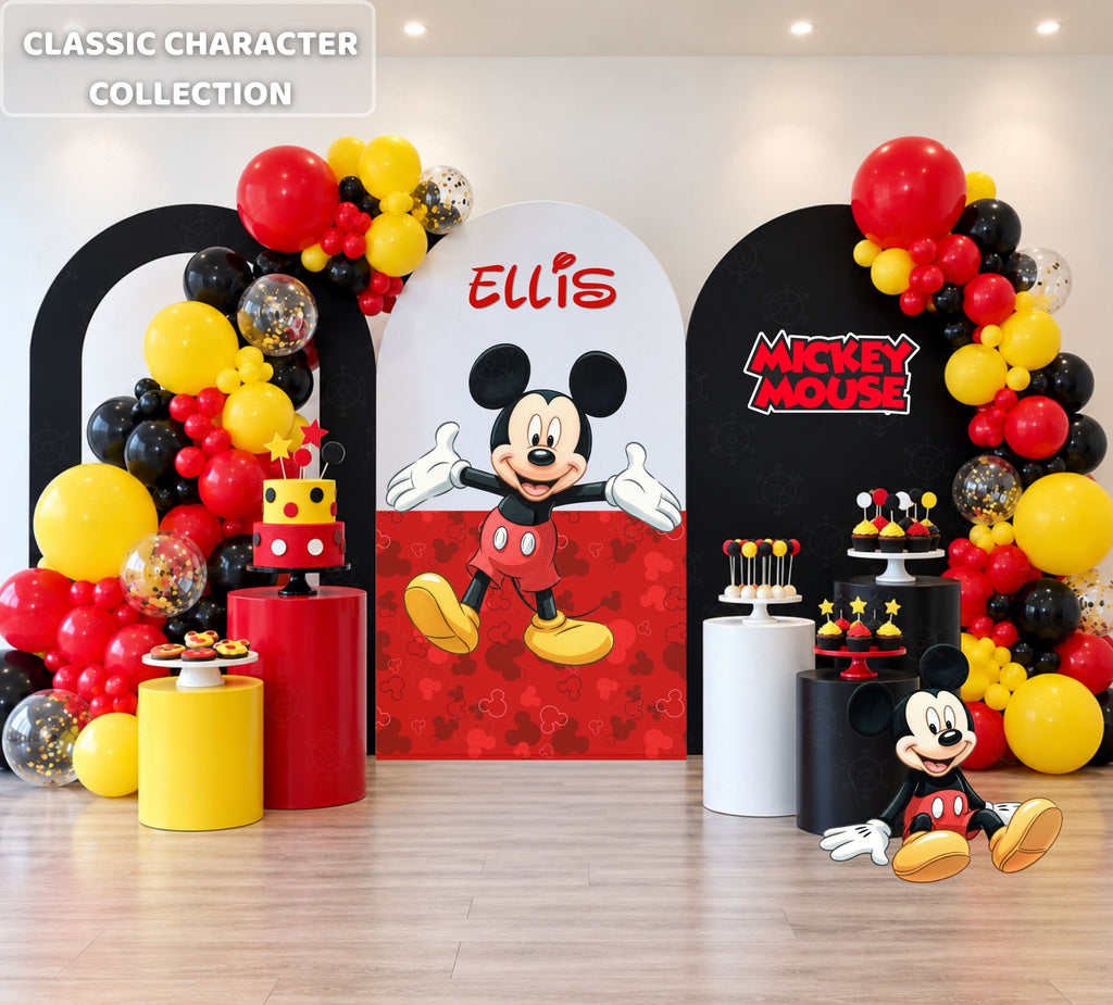 Classic mouse birthday backdrop with red, black and white arch panels, balloon garland, personalized name and matching party cutouts.