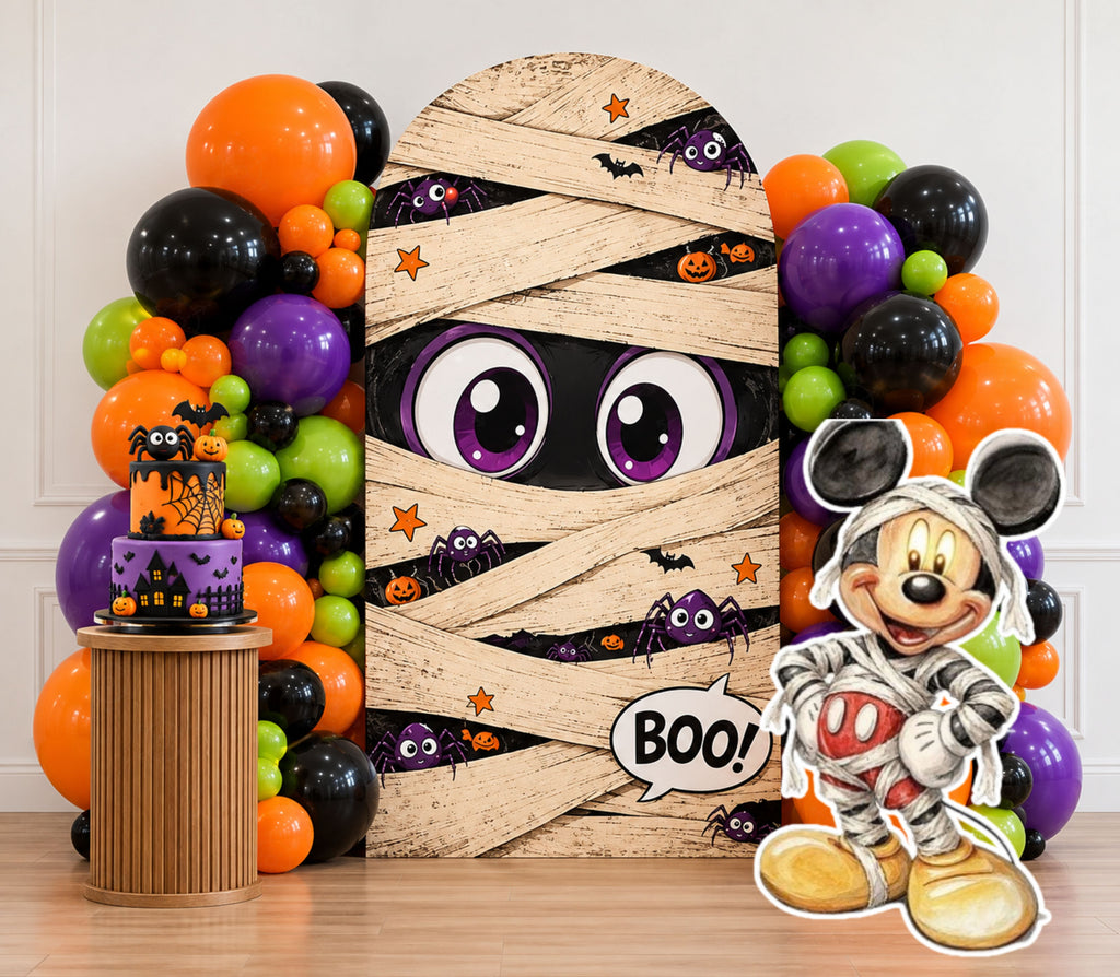 Mummy-inspired spooky birthday backdrop with orange purple green and black balloons, themed cake display and matching character cutout.