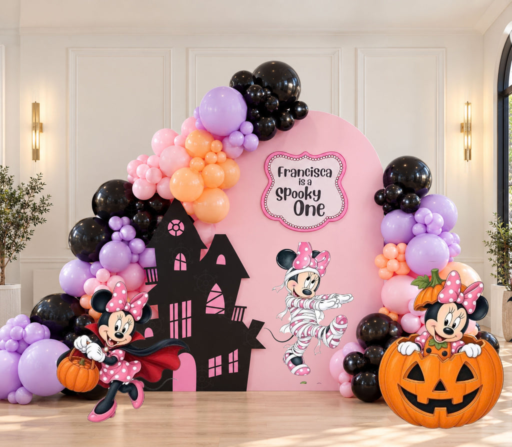 Pink spooky character birthday backdrop with black purple and peach balloons, haunted house silhouette, pumpkin accents and matching themed cutouts.