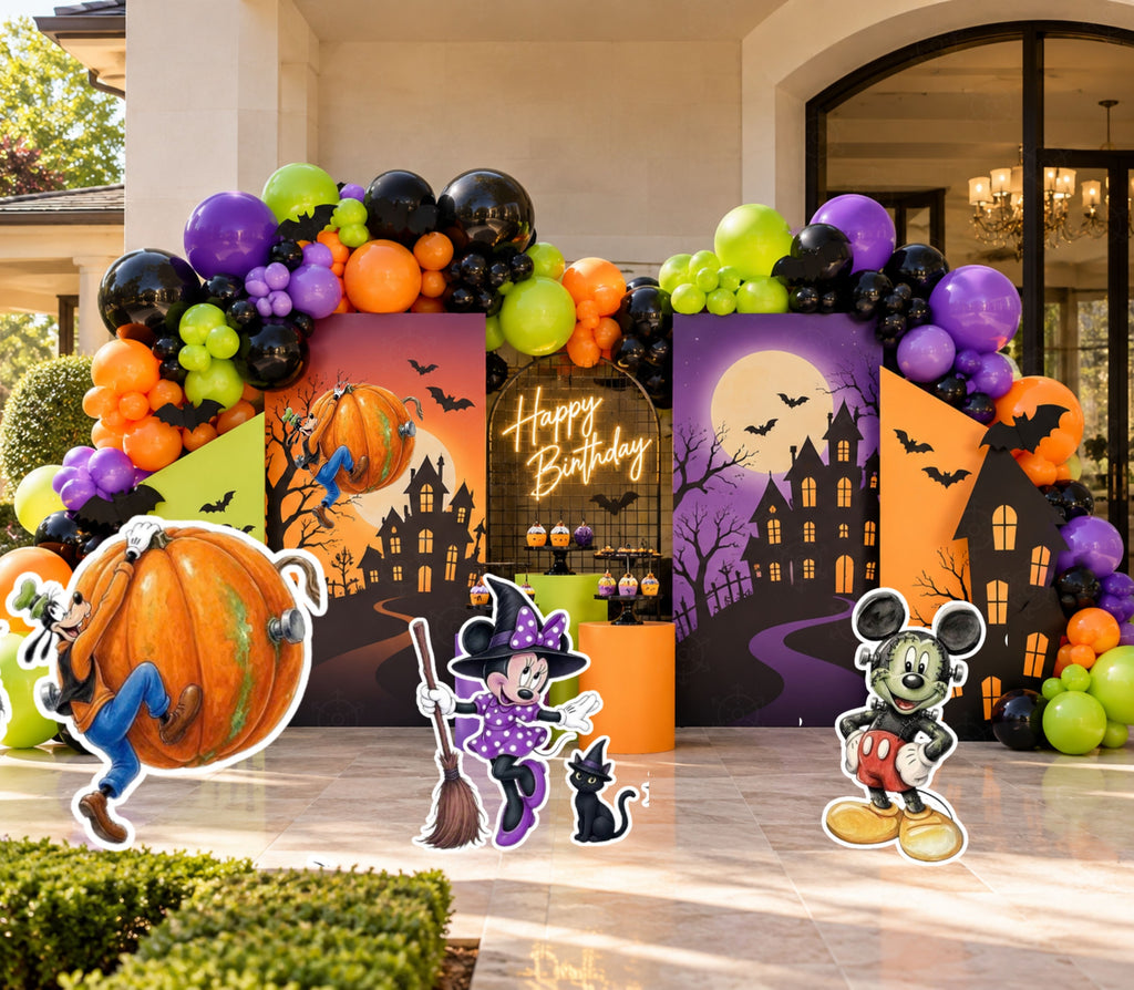 Spooky birthday backdrop set with haunted house panels, orange purple green and black balloons, pumpkin decor and matching character cutouts.